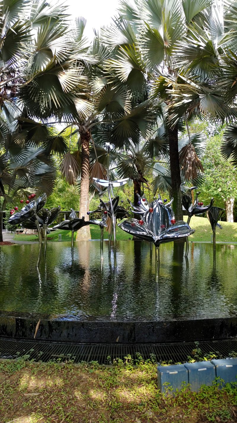 a fountain in the sky forest area with metal flowers with red stamen