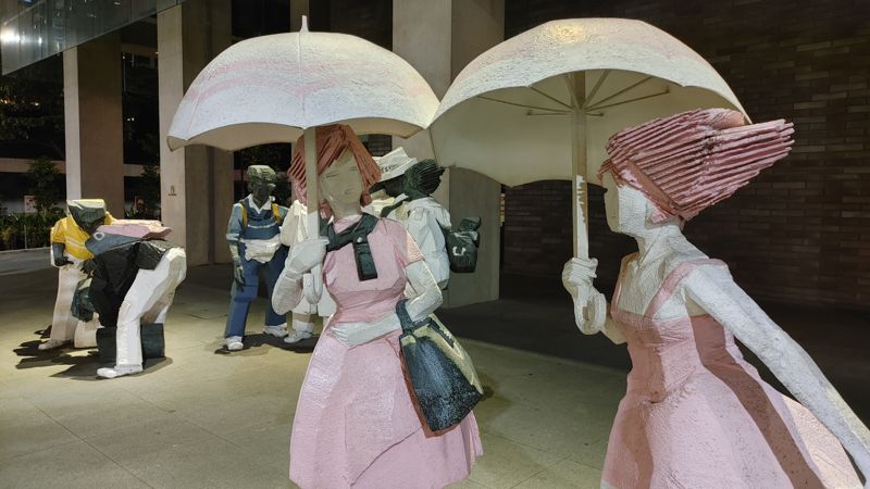 statue art of two girls in pink dresses with umbrellas and male figures in the background